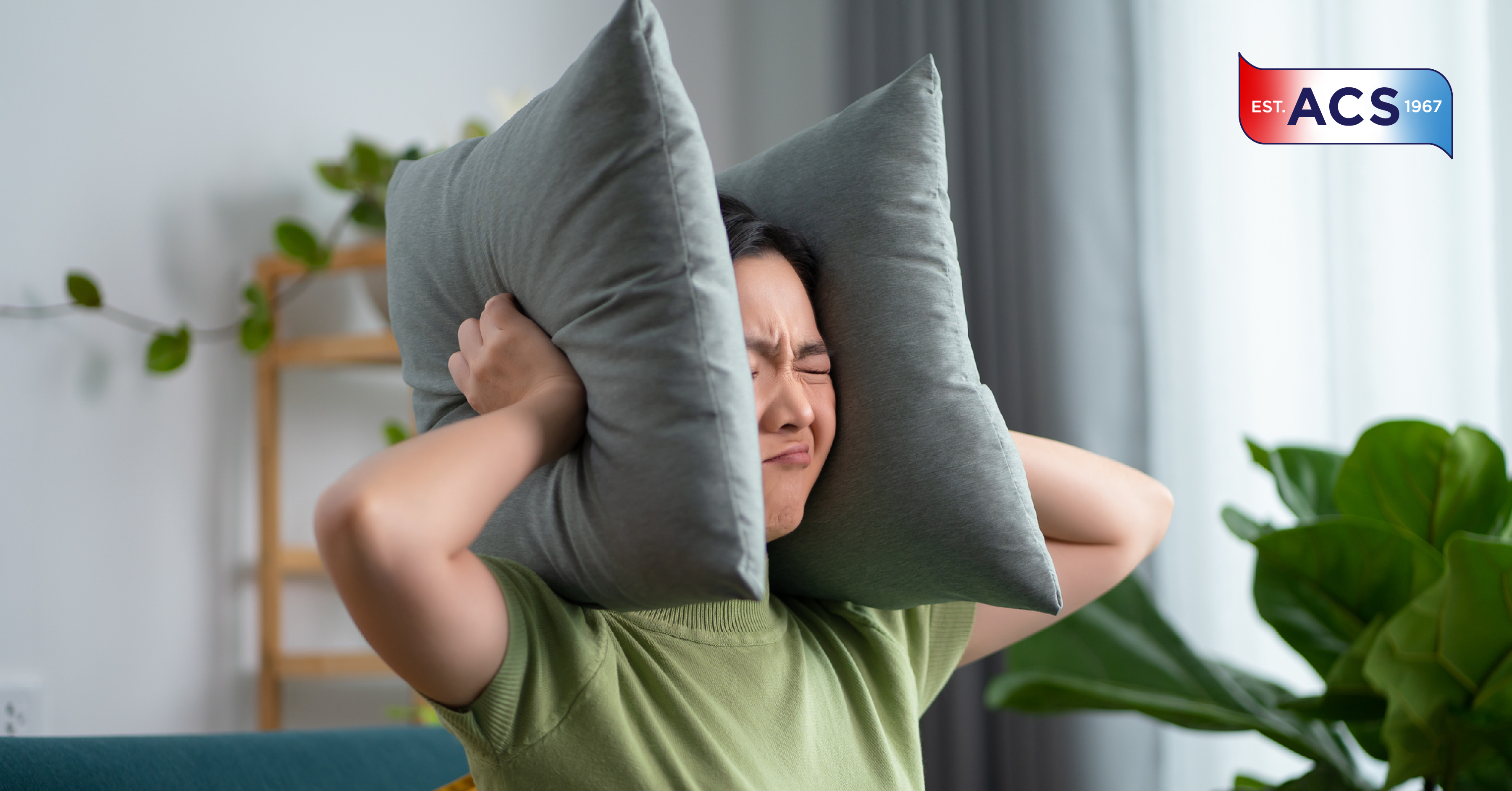 Woman holding pillows to her head to stop hearing annoying HVAC unit noise