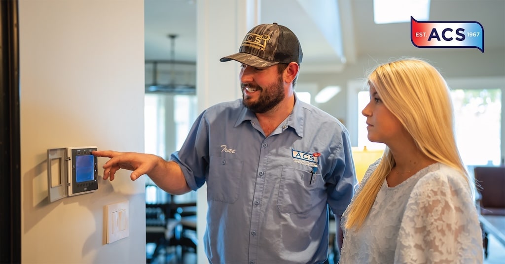 AC repair man looking at thermostat with female home owner