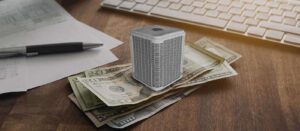 A small SEER air purifier sits on a stack of U.S. dollar bills on a desk in Greensboro, next to a pen, papers, and a computer keyboard.