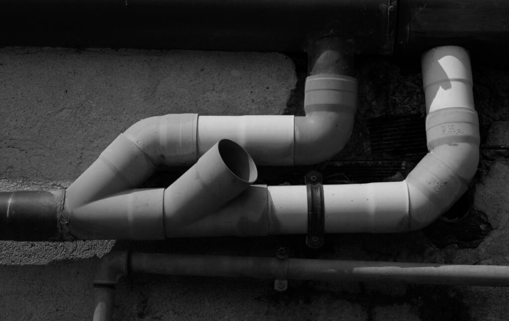 A set of white PVC pipes connected in a complex arrangement on an exterior wall in Laurens County, GA, with visible joints and brackets.