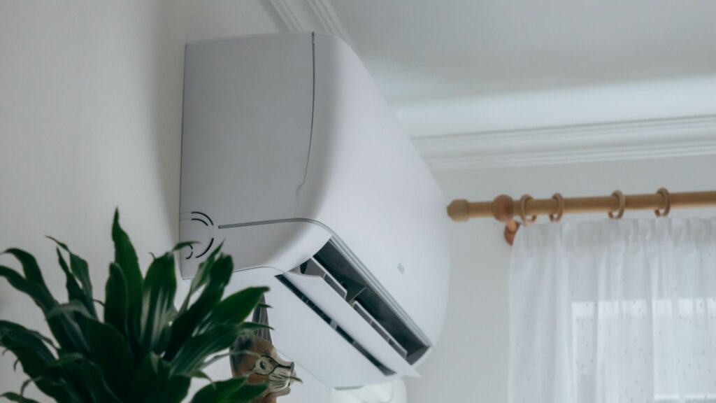 Wall-mounted air conditioning unit installed above a plant near a window with sheer curtains and a curtain rod, providing cool comfort to your Conyers home.
