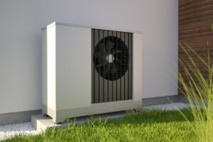 Outdoor heat pump unit installed on a concrete pad next to a building in Covington, with grass and gravel in the foreground. 2026 Heating Tax Credits